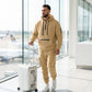Krovax Tech Fleece Urban Utility Set in beige Sand Dune worn by a man in an airport, showing the half-zip hoodie and cargo joggers with tactical pockets.