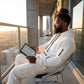 Krovax Tech Fleece Urban Utility Set in white, seated side view showing the tactical sleeve pocket and cargo joggers on a city balcony.