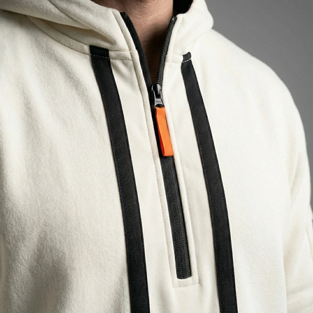 Close-up of Krovax Tech Fleece hoodie in beige showing half-zip neckline with orange pull tab and black tactical taping details.