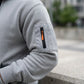 Krovax Tech Fleece hoodie in grey showing the tactical zippered sleeve pocket with orange pull tab and ribbed cuff detail.