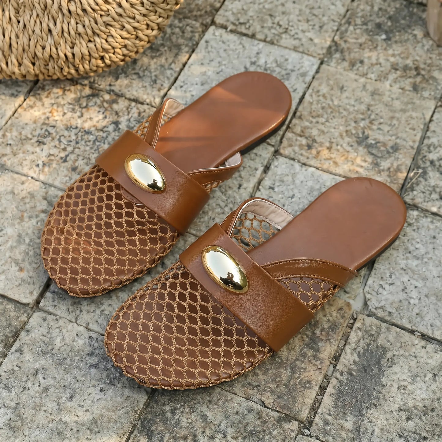 Warm brown Kryxos mesh pointed-toe flat mules with gold oval hardware and faux leather strap, shown on a stone surface with natural light.