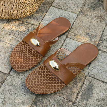 Warm brown Kryxos mesh pointed-toe flat mules with gold oval hardware and faux leather strap, shown on a stone surface with natural light.