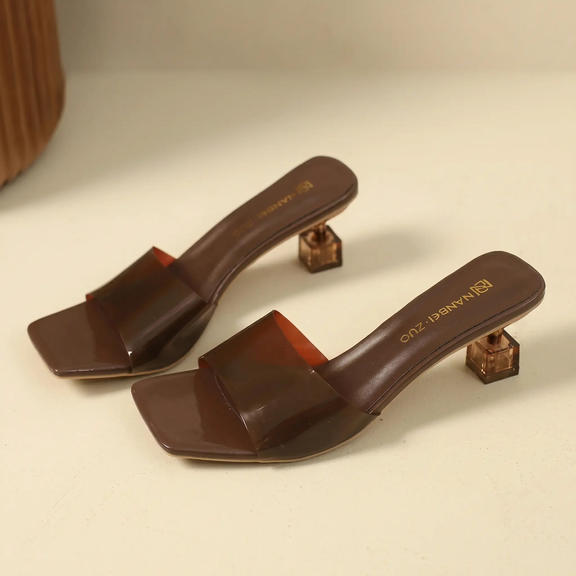 Brown square-toe slip-on mule sandals with a transparent geometric block heel and a single semi-transparent strap.