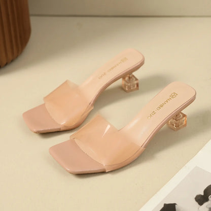 Nude pink slip-on mule sandals featuring a square toe, a single semi-transparent frosted strap, and a clear geometric block heel.