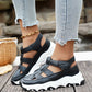 Kryzen black chunky platform sandals with white soles, worn by a model with distressed jeans and a gold anklet on a wooden surface.