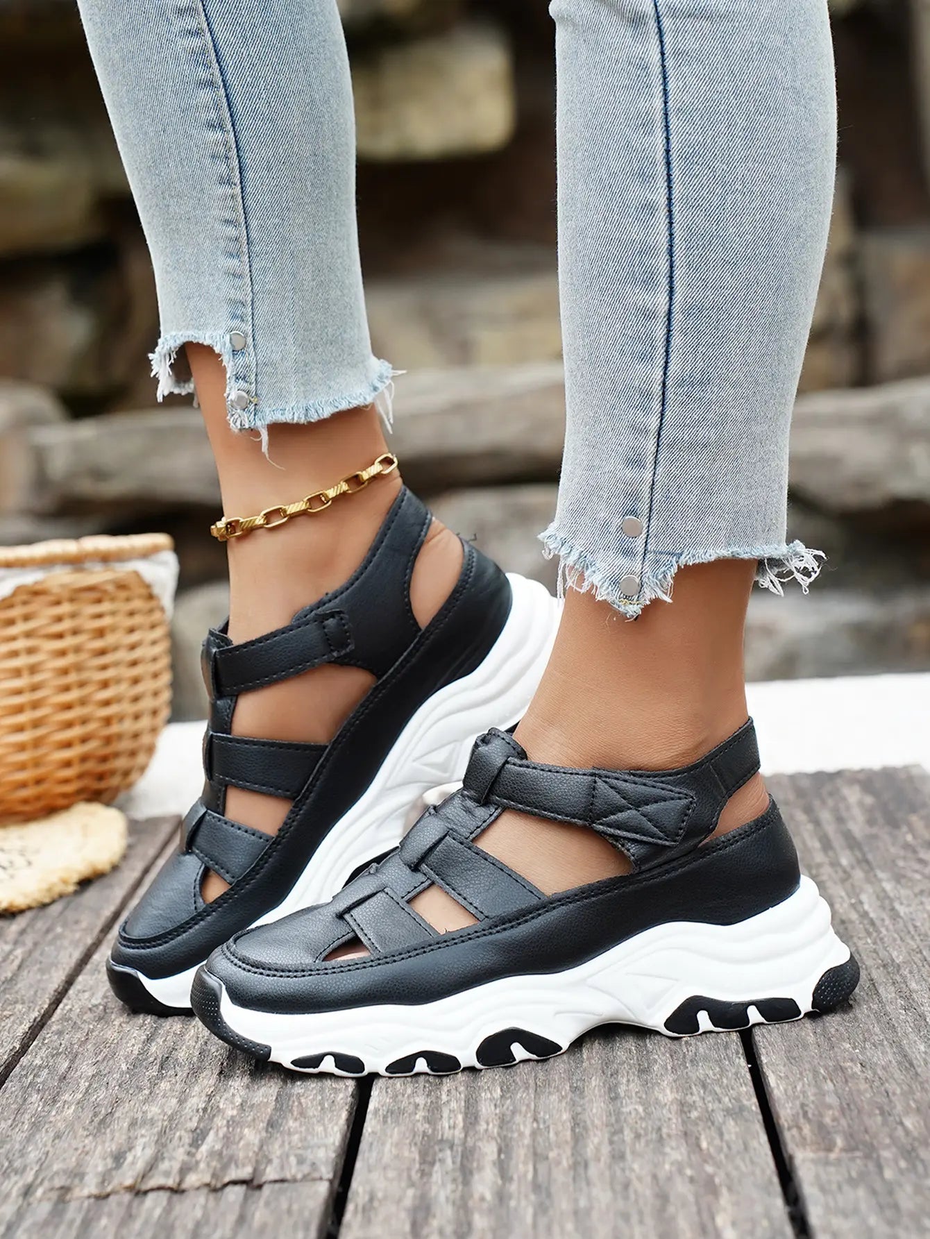 Kryzen black chunky platform sandals with white soles, worn by a model with distressed jeans and a gold anklet on a wooden surface.
