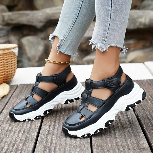 Black sporty chic Kryzen sandals with a chunky platform sole and open back, styled with distressed denim jeans on a wooden surface.