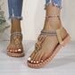 Bohemian flat thong sandals featuring intricate floral bead embellishments and tribal-patterned woven straps, worn on a model's feet with distressed jeans and a beaded ankle bracelet.