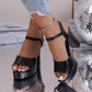Kylos black platform high heel sandals with a fish-mouth peep-toe and ankle strap, styled on feet with distressed denim jeans and a sparkling charm accent, set against a reflective surface with disco ball decor.