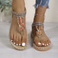 Kylos desert khaki bohemian flat thong sandals for women, featuring intricate bead and floral embellishments, tribal woven straps, and a comfortable elasticated heel strap on a light grey wooden floor.