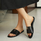 Woman's feet wearing black Kyluxa leather slide sandals with a gold metallic V logo emblem, displayed on a neutral tiled floor.
