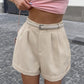 Elegant wide-leg linen-blend shorts in soft beige, worn by a model with a coordinating light grey belt and rolled cuffs, showcased in a chic outdoor setting.