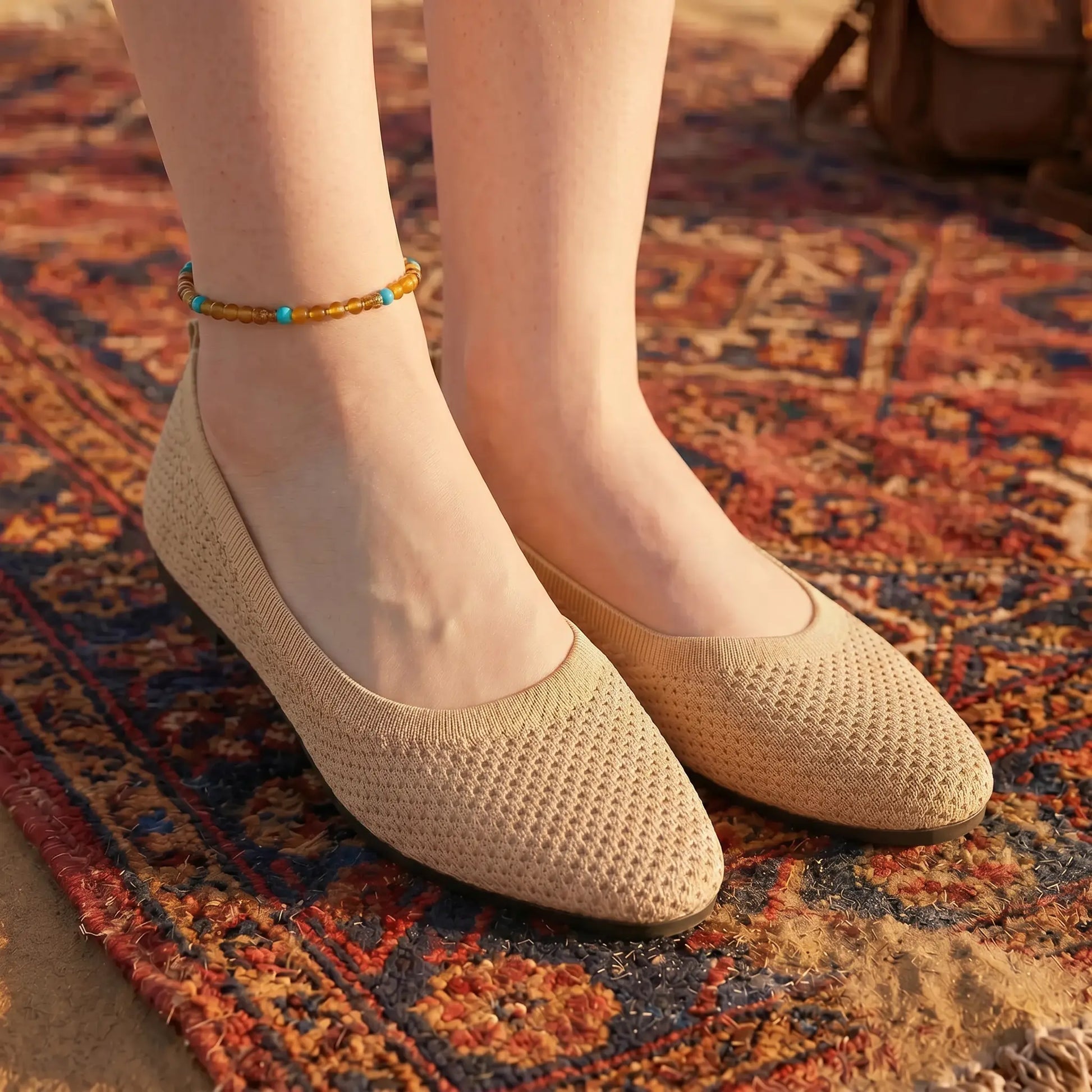 Kyneth Oat Beige Breathable Knit Pointed Flats worn on feet, showcasing the woven texture and comfortable design, placed on a vibrant bohemian-patterned rug outdoors.