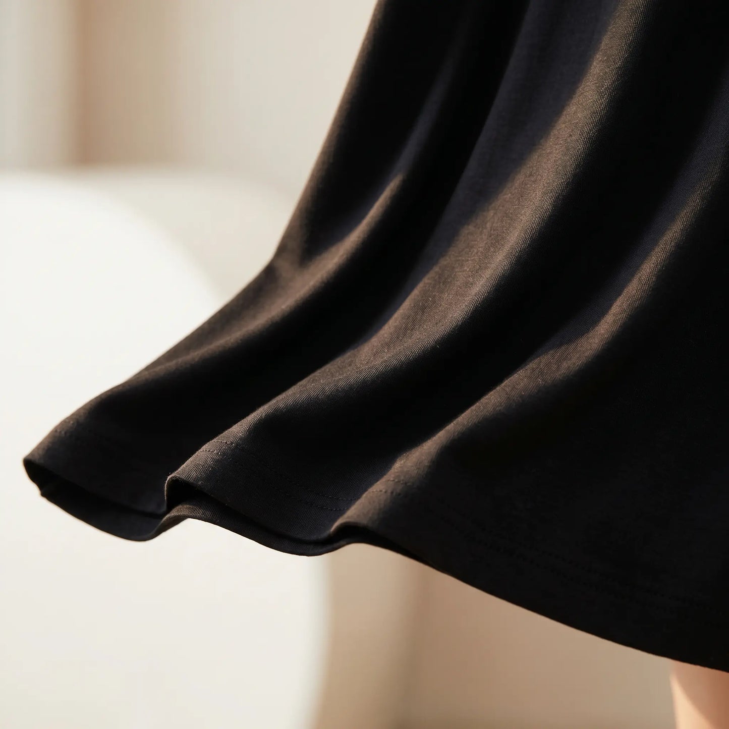 Close-up of the flowing A-line hem of the Kynso black premium modal slip dress, showcasing the soft micro-knit texture and elegant drape in natural light.
