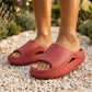 Kynso Platform Lounge Slides in rich Carmine Red, made from molded EVA, worn on feet walking on a gravel path amidst a lush garden.
