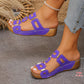 Woman's feet wearing purple Kyorin platform wedge sandals with geometric gold embellishments and white contrast stitching, shown on a grey surface.