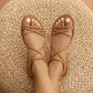Kyrok warm camel flat sandals with bohemian tubular crossover straps, worn on feet against a natural woven background. Premium vegan leather, round toe.