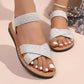 Kythos embellished flat sandals in sparkling white, featuring shimmering crossover straps, an elasticated ankle strap, and an open-toe, open-heel design.
