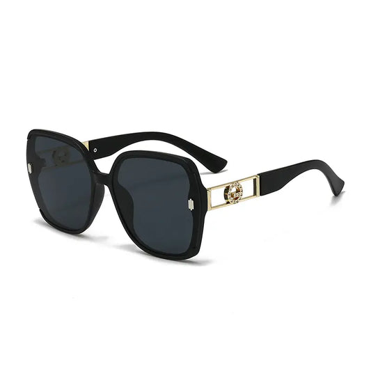 Kyzira luxury oversized square sunglasses in black with gold-tone geometric temple detailing and dark gradient lenses, shown from a three-quarter angle.
