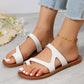 White Kyzmiv open-toe slide sandals with asymmetrical straps, featuring white contrast stitching on the flat sole, worn by a model with a gold anklet.