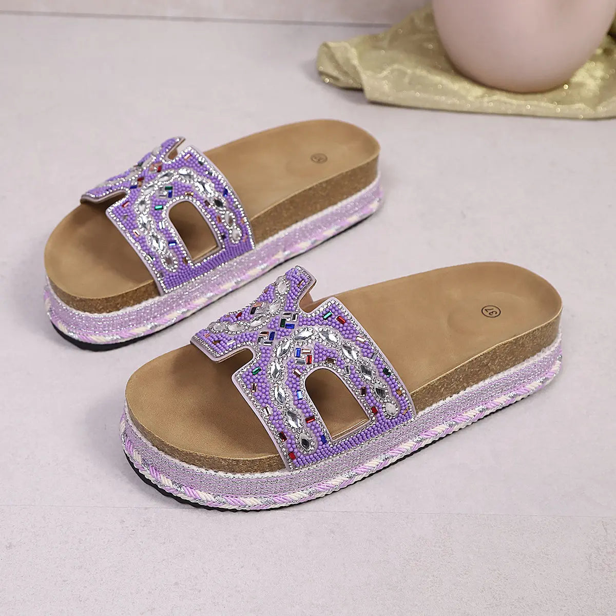 Lavender embellished platform slide sandals with U-shaped cutouts, detailed with iridescent beads and rhinestones, featuring a cork footbed and woven midsole.
