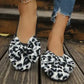 Women's leopard print ballet flats with large, layered bows on the vamp, shown worn on feet with ripped denim jeans on a wooden surface, ideal for casual chic styling.