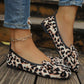 Women's leopard print ballet flats featuring a large layered bow detail, worn with ripped jeans and a silver anklet on a wooden surface.