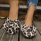 Women's leopard print ballet flats featuring large, layered bows on the vamp, shown worn with distressed jeans on a wooden surface.