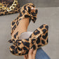 Close-up of leopard print wedge sandals with oversized bows, worn on a woman's feet, showcasing the peep-toe and platform heel on a grey studio background.