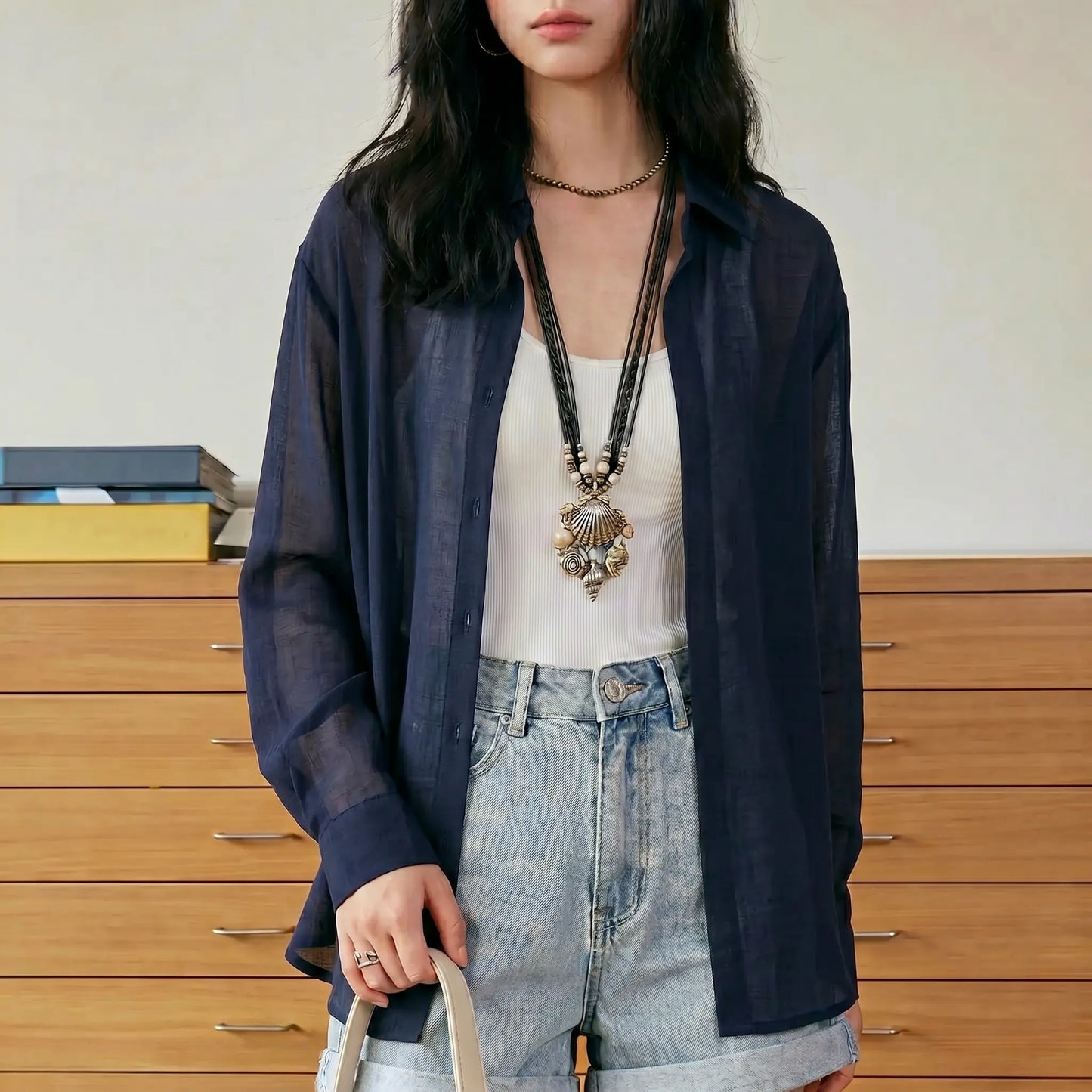 Female model wears a Kynzor Lightweight Tencel button-down blouse in Midnight Birch Blue, worn open over a white tank top and light denim shorts, featuring a pointed collar and relaxed fit, styled in an indoor setting.