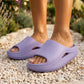 Lilac Purple Kynso platform lounge slides in molded EVA, worn by a person on a light pebble path. The open-toe slippers feature a thick 4.0cm sole, subtle side cutout, and ergonomic design.