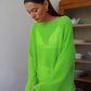 Model wearing Zomari's vibrant lime green sheer open-knit bell sleeve sweater, featuring a wide boat neckline and dropped shoulders, in an elegant indoor setting.
