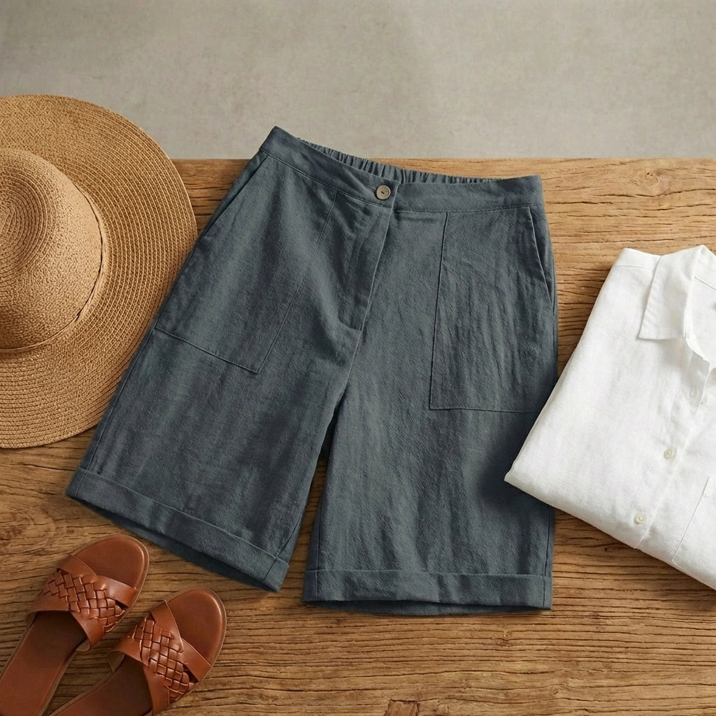 Linara high-waisted linen blend Bermuda shorts in Charcoal Slate, flat lay view showing deep patch pockets and cuffed hems styled with summer accessories.