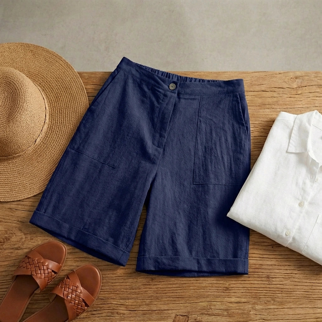 Linara high-waisted linen blend Bermuda shorts in navy blue, flat lay view styled with a straw hat and leather sandals.