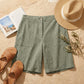 Linara High-Waist Linen Blend Bermuda Shorts in Sage Green — flat lay view with summer accessories on stone background.