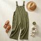 Luvana cotton linen overalls in olive green, displayed in a flat-lay lifestyle setting with a straw hat, sandals, and accessories.