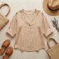 Luvana linen blend blouse in beige with V-neck and single-button detail, displayed in a flat-lay with a straw hat and bag.
