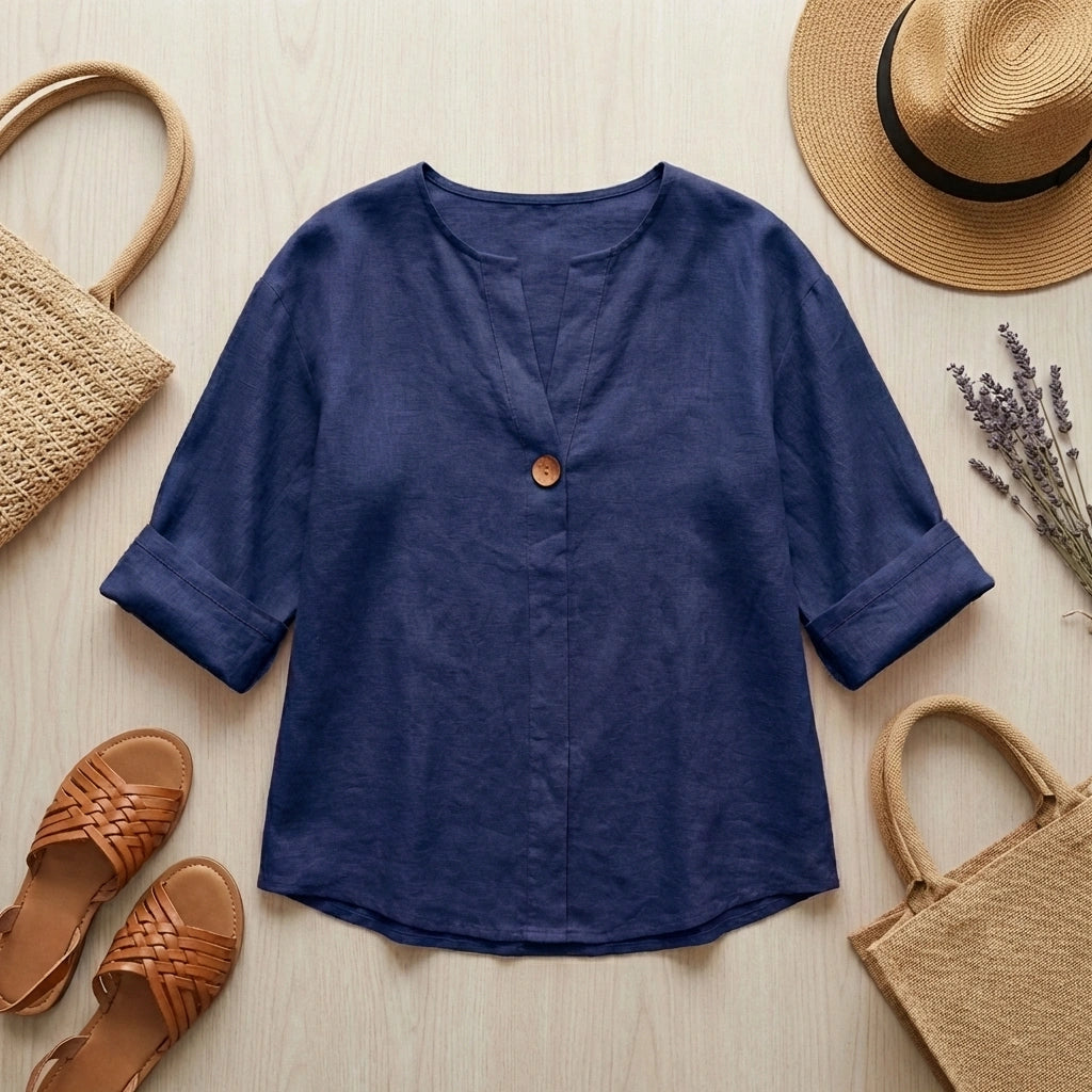 Luvana navy blue linen blend blouse with V-neck and wooden button, displayed in a summer flat-lay with a straw hat and sandals.