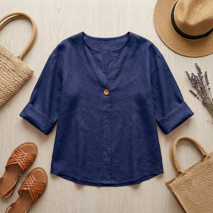 Luvana navy blue linen blend blouse with V-neck and wooden button, displayed in a summer flat-lay with a straw hat and sandals.