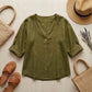Luvana olive green linen blend blouse in a flat-lay arrangement with summer accessories including a straw hat, sandals, and a tote bag.