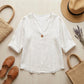 Luvana white linen blend blouse with V-neck, styled in a summer flat-lay with a straw hat, bag, and sandals on a wooden surface.