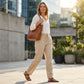 Luvana linen blend trousers in desert sand with elastic waist worn by a woman walking in a city, showing a relaxed straight-leg fit.