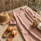 Luvara linen-look V-neck dress in dusty rose, laid flat on stone with a straw hat and dried flowers for a summer coastal aesthetic.