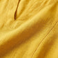 Close-up of the golden ochre linen-look v-neck dress, highlighting the textured fabric weave and clean neckline stitching.