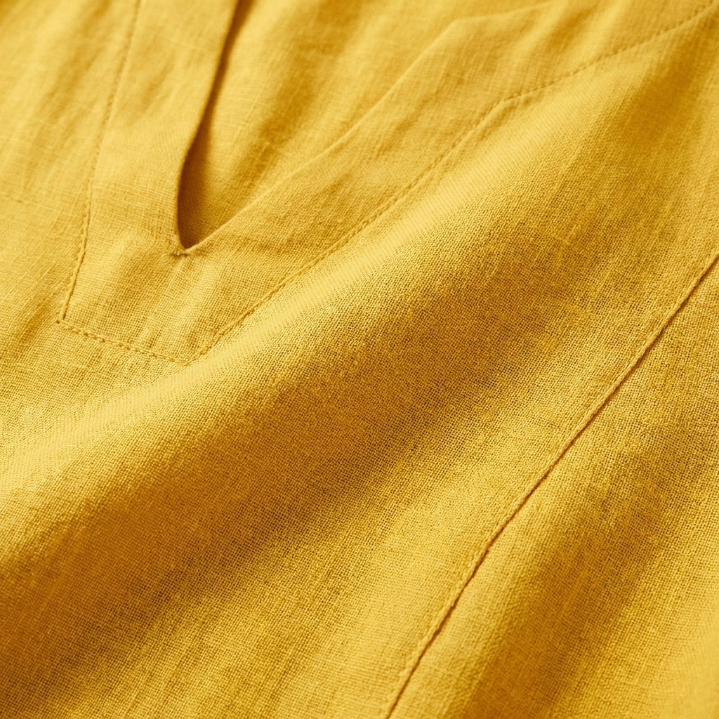 Close-up of the golden ochre linen-look v-neck dress, highlighting the textured fabric weave and clean neckline stitching.