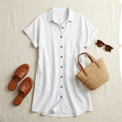 Luvara white linen shirt dress styled with brown woven slides, a straw tote bag, and sunglasses on a neutral textured background.