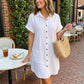 Luvara white linen shirt dress for women, mini length with tortoiseshell buttons and cuffed sleeves, worn in an outdoor cafe setting.