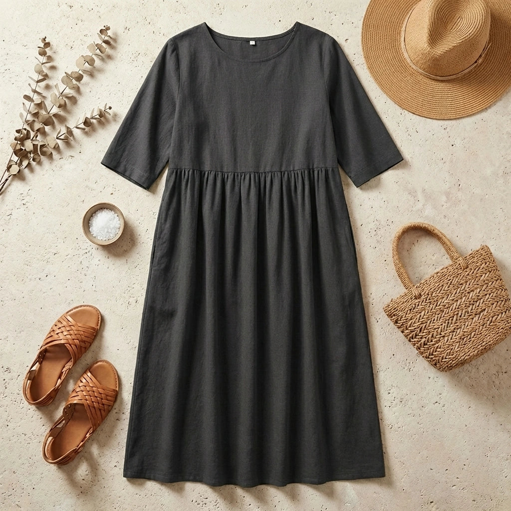 Luvia cotton linen midi dress in charcoal grey, styled as a flat-lay with a straw hat, sandals, and handbag on a neutral surface.