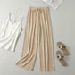 Luvia wide leg pleated plissé trousers in champagne beige, styled in a flat-lay with a white camisole and gold necklace.
