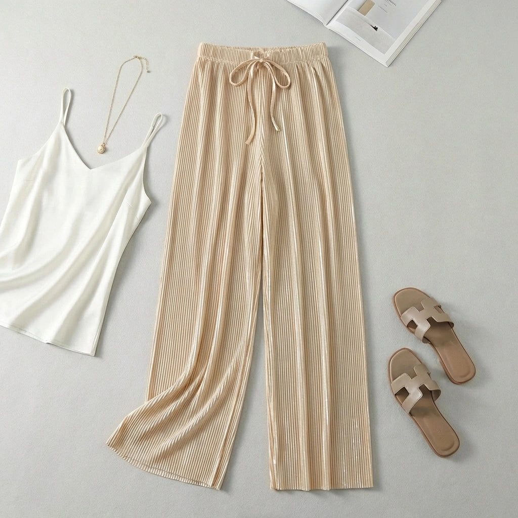 Luvia wide leg pleated plissé trousers in champagne beige, styled in a flat-lay with a white camisole and gold necklace.